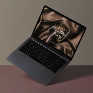 Peut inclure: Un ordinateur portable gris avec un clavier noir et un écran affichant les mots "Charming Poem" sur un fond de tissu marron. L'ordinateur portable est incliné sur un fond bicolore marron et rose.
