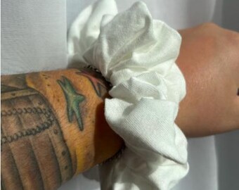 May include: White fabric scrunchie hair tie. The scrunchie is made of soft, white fabric and is tied in a knot.