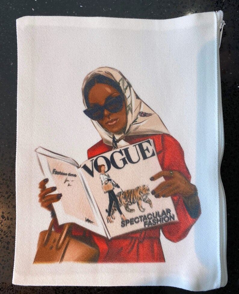 May include: A white zippered pouch with a colorful illustration of a woman wearing a headscarf and sunglasses, holding a copy of Vogue magazine with the text "SPECTACULAR FASHION".