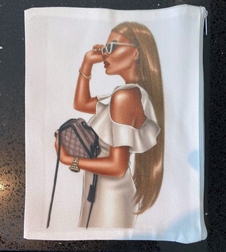 May include: A white zippered pouch with a printed image of a woman wearing a white dress, sunglasses, and a small purse. The woman has long brown hair.