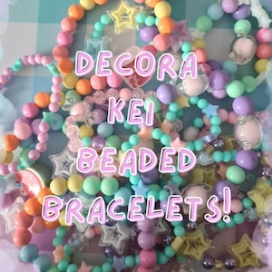 Könnte beinhalten: Eine Sammlung farbenfroher Perlenarmbänder in Pastelltönen von Rosa, Blau, Gelb, Grün und Lila. Einige Armbänder haben stern- und herzförmige Anhänger. Der Text "DECORA KEI BEADED BRACELETS!" ist im Bild zu sehen.