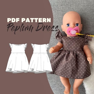 Könnte beinhalten: Eine Puppe trägt ein braunes Peplum-Kleid mit weißen Punkten und Rüschenärmeln. Die Puppe hat einen rosa Schnuller und liegt auf einer grauen Oberfläche. Das Bild zeigt auch ein Schnittmuster für das Kleid mit dem Text "PDF Pattern Peplum Dress".