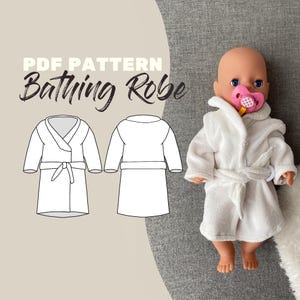 Könnte beinhalten: Ein weißer Frottee-Bademantel für eine Puppe mit Kapuze und Bindegürtel, getragen von einer Puppe mit einem rosa Schnuller. Das Bild zeigt auch eine Strichzeichnung des Bademantels mit dem Text "PDF PATTERN Bathing Robe".