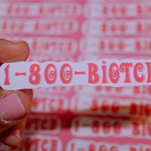 May include: A white sticker with pink text that reads "1-800-BIOTCH" in a retro font. The sticker is being held by a hand.