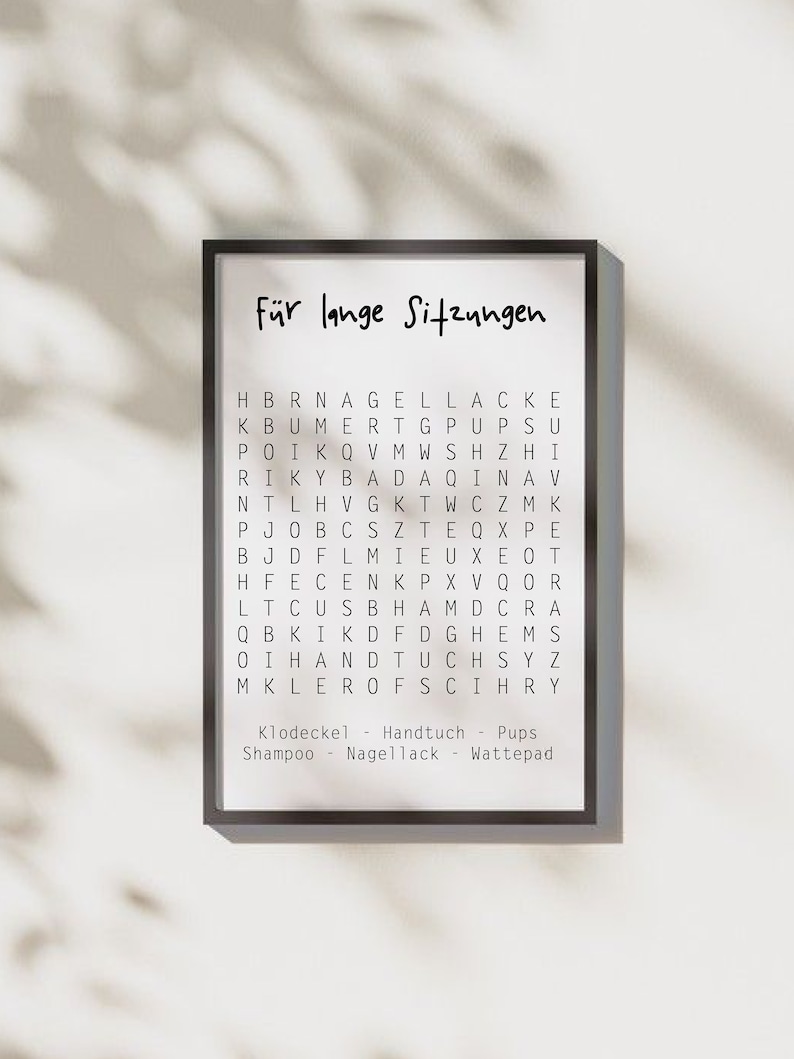 May include: A black framed print with the text "F&uuml;r lange Sitzungen" in white. The print features a word search puzzle with the words "Klodeckel", "Handtuch", "Pups", "Shampoo", "Nagellack", and "Wattepad" listed below.