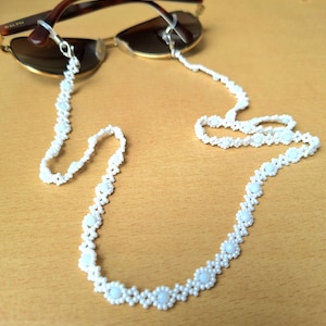 May include: White beaded eyeglass chain with small white beads and larger white beads in a flower shape.