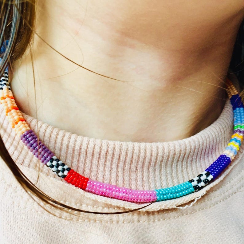 May include: A colorful beaded necklace with alternating patterns of black and white, pink, blue, purple, orange, yellow, and turquoise beads.