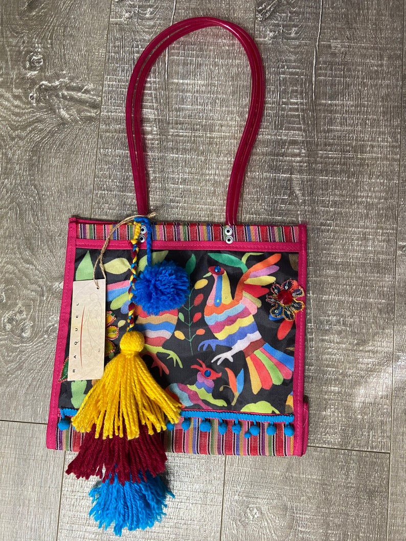 Pode incluir: Uma bolsa tote preta com um design bordado colorido de p&aacute;ssaros e flores. A bolsa tem uma al&ccedil;a rosa e vem com tr&ecirc;s borlas coloridas.