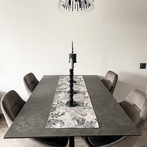 Puede incluir: Una mesa de comedor rectangular de color gris oscuro con una base de metal negro y seis sillas tapizadas en gris. Un camino de mesa con estampado blanco y gris con un candelero negro en el centro.