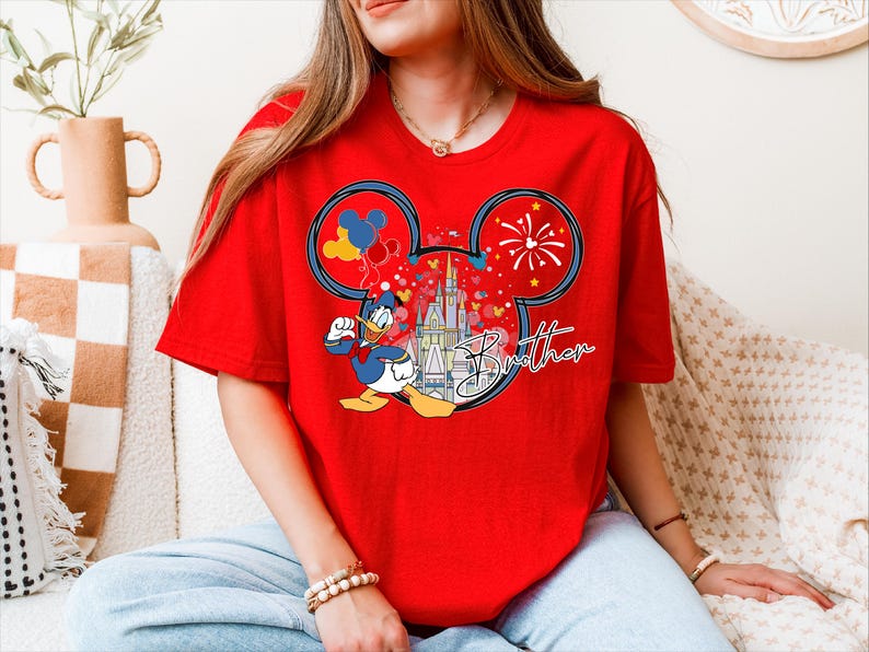 A woman wearing a red t-shirt with a Mickey Mouse design and fireworks on it, sitting on a couch.