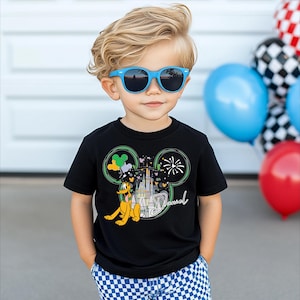 A young boy wearing a black t-shirt with a Mickey Mouse design and blue sunglasses, standing in front of a wall with balloons.