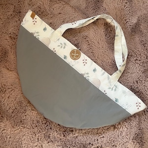 Könnte beinhalten: Graue Tragetasche mit halbkreisförmigem Design. Der obere Teil hat einen weißen Stoff mit Blumen- und Vogelmuster. Sie hat einen passenden weißen Griff und ein kleines, rundes, braunes Etikett mit "Handmade".