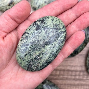 May include: A collection of green and black serpentine palm stones. The stones are smooth and polished, with a variety of patterns and swirls.