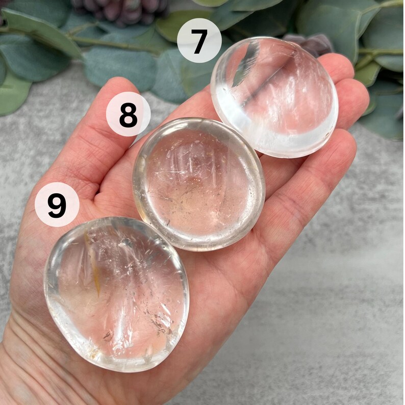 May include: Three clear quartz crystal palm stones, also known as worry stones, in various sizes. The stones are smooth and polished, with a translucent appearance.