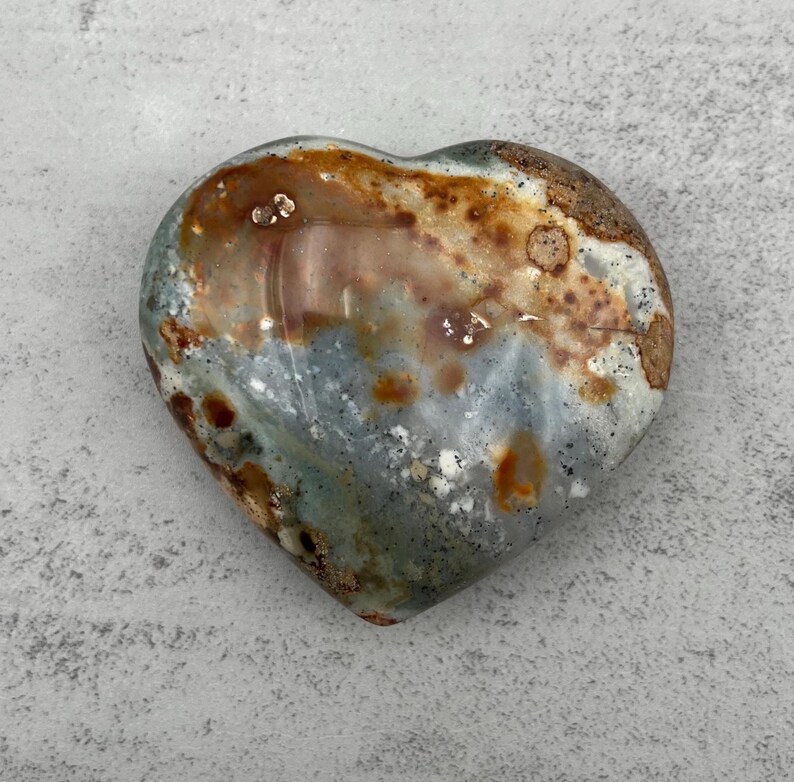 May include: A heart-shaped polished stone with a mix of brown, gray, and white colors. The stone has a natural, organic look.