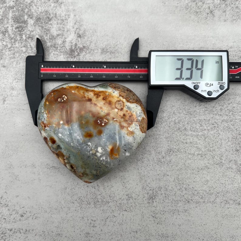 May include: A heart-shaped green, brown, and white agate stone measuring 3.34 inches in length.