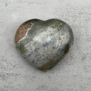 May include: A heart-shaped polished stone with a gray, white, and brown marbled pattern.