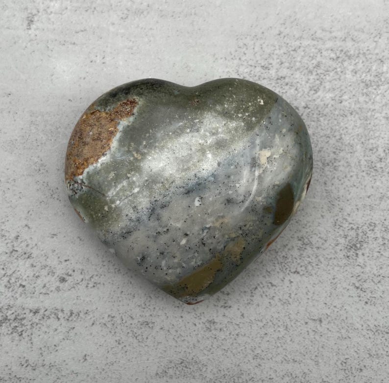 May include: A heart-shaped polished stone with a gray, white, and brown marbled pattern.