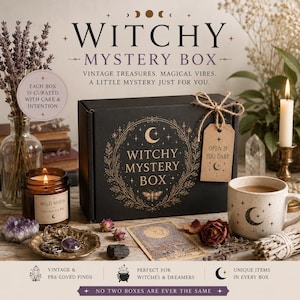 May include: A black rectangular box labelled WITCHY MYSTERY BOX with gold celestial graphics, tied with twine and a tag reading OPEN IF YOU DARE. It is surrounded by a candle, a ceramic mug with a moon design, a tarot card, crystals, and dried flowers.