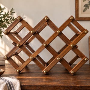 May include: A brown wooden wine rack featuring an expandable accordion-style lattice design. The structure is composed of intersecting wooden slats connected by round brass-coloured metal rivets at each junction, creating a series of diamond-shaped openings.