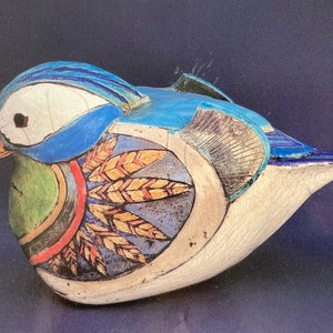 May include: A ceramic bird sculpture with a blue, white and green painted design. The bird has a long beak and a stylised wing pattern.