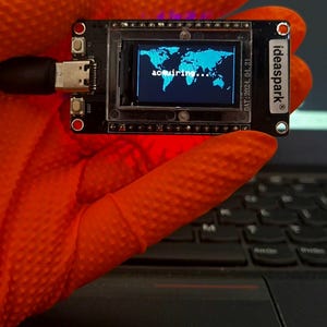 May include: A black rectangular microcontroller board with a small screen displaying a blue world map and the text "acquiring...". The board features a USB-C port, two buttons, and the printed text "ideaspark" and "DAT: 2024.04.21" on its surface.