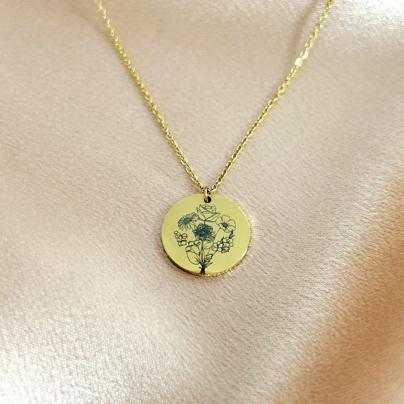 Peut inclure: Un collier dor&eacute; dot&eacute; d'un pendentif circulaire grav&eacute; d'une illustration botanique d&eacute;licate aux lignes sombres repr&eacute;sentant un bouquet de fleurs. Le pendentif est suspendu &agrave; une fine cha&icirc;ne dor&eacute;e assortie compos&eacute;e de petits maillons uniformes.