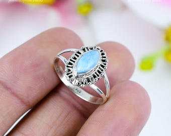 May include: A sterling silver ring featuring a light blue oval gemstone. The gemstone is set in a decorative, dark-toned bezel. The ring has a split shank design and is held in a hand.