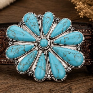 May include: A brown leather belt featuring an intricate floral embossed pattern and a large, circular silver-toned buckle. The buckle is adorned with a central turquoise stone surrounded by twelve teardrop-shaped turquoise cabochons.