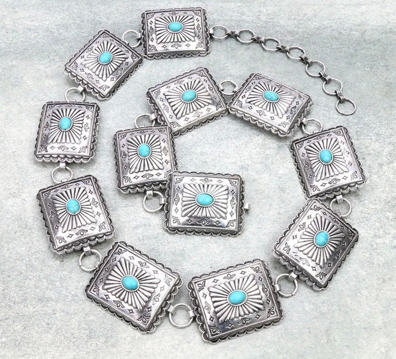 May include: A silver belt with turquoise stones set in square-shaped metal pieces. The belt is made of a chain with links that connect the metal pieces.