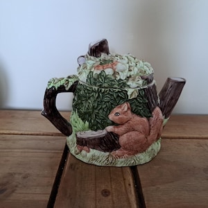 以下が含まれることがあります： 森をテーマにしたセラミックティーポット。 ティーポットは切り株の形をしており、側面に茶色のリスがいます。 蓋は葉と花で飾られています。 ハンドルと注ぎ口は木の枝のようにデザインされています。