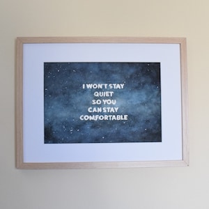 Puede incluir: Una impresión enmarcada con un fondo de galaxia acuarela azul y texto blanco que dice "No me quedaré callado para que puedas estar cómodo."
