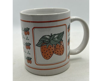 May include: White ceramic mug with a strawberry design. The mug features a large strawberry illustration with green leaves and a border of smaller strawberry patterns. The handle is curved and the mug has a red trim.