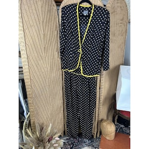 May include: A black polka dot suit with a yellow trim. The suit includes a blazer with a single button closure and matching wide-leg pants. The outfit is displayed on a hanger against a woven background.