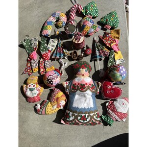 May include: A collection of handmade Christmas ornaments in various shapes and sizes. Includes candy canes, trees, dolls, hearts, and balls, all crafted from colorful patchwork fabric. Some ornaments have decorative details like beads and ribbons.
