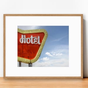 以下が含まれることがあります： ヴィンテージホテルの看板の額装プリント。看板は赤色で、白い「Hotel」の文字が黄色い縁取りで囲まれています。背景は雲のある青い空です。プリントは木製のフレームに入っています。