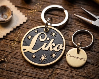 May include: A round brass keychain featuring the name Liko in raised script lettering against a textured black background with star accents, accompanied by a smaller circular brass tag engraved with the text CharmingcraftUS on a metal ring.