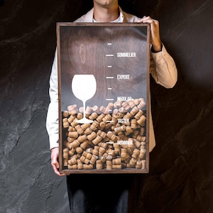 Könnte beinhalten: Ein rechteckiger Holzrahmen gefüllt mit Naturkorken, mit einer weißen Weinglasgrafik und aufgedruckten Textstufen: BEGINNER, TASTER, REGULAR, EXPERT und SOMMELIER. Unten befindet sich das aufgedruckte Datum 16 | 09 | 2025.
