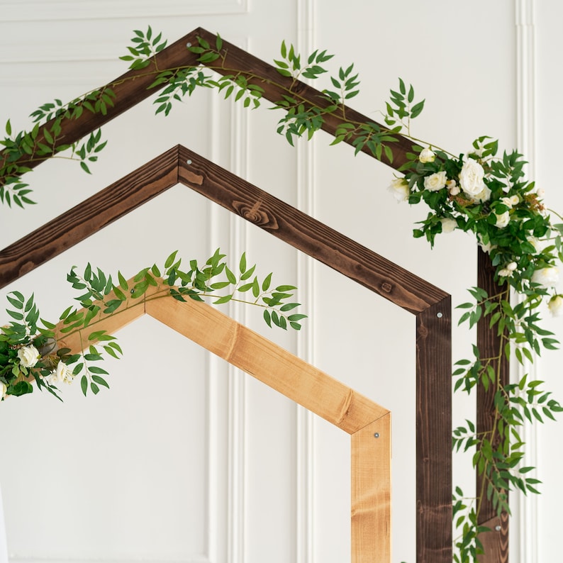 May include: A wooden archway decorated with greenery and white flowers. The archway is made of two pieces of wood, one brown and one natural wood.