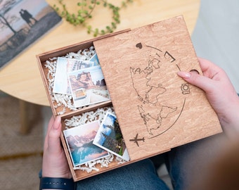 May include: A wooden box with a world map design and a hinged lid. The box is open and contains several small photos. The photos are of various travel destinations.