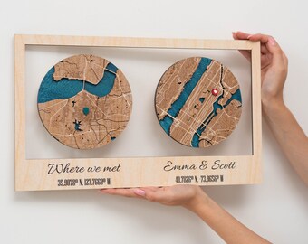 May include: A wooden framed artwork featuring two circular maps with teal blue water features. The maps are engraved with city details and coordinates. The text "Where we met" and "Emma & Scott" are displayed below the maps.