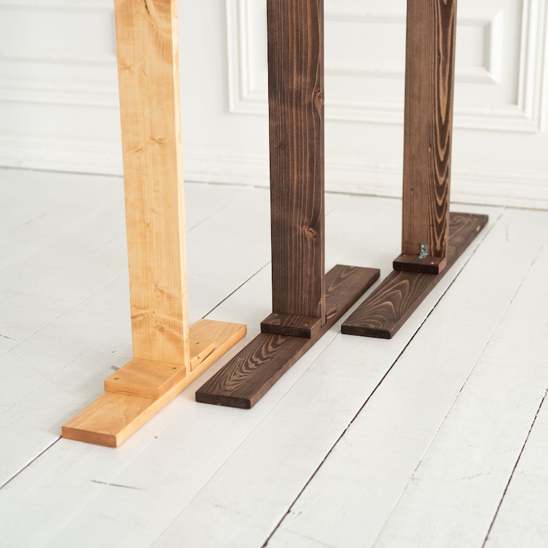 May include: Three wooden stands, one natural wood and two stained dark brown, with a simple L-shaped design. The stands are on a white wood floor.