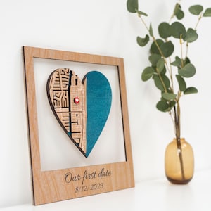 Puede incluir: Adorno de pared de madera en forma de coraz&oacute;n con marco. El coraz&oacute;n est&aacute; dividido en dos partes: una con un dise&ntilde;o tallado y otra turquesa. Un peque&ntilde;o alfiler rojo en forma de coraz&oacute;n est&aacute; en el centro. El texto "Our first date 8/12/2023" est&aacute; impreso en el marco.