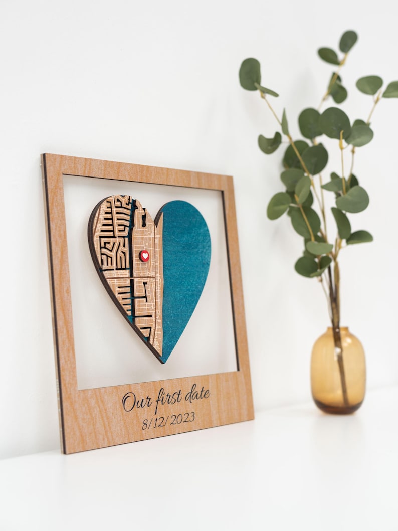Puede incluir: Adorno de pared de madera en forma de coraz&oacute;n con marco. El coraz&oacute;n est&aacute; dividido en dos partes: una con un dise&ntilde;o tallado y otra turquesa. Un peque&ntilde;o alfiler rojo en forma de coraz&oacute;n est&aacute; en el centro. El texto "Our first date 8/12/2023" est&aacute; impreso en el marco.