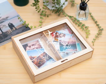 May include: A wooden box with a clear lid, divided into two compartments. Each compartment has a world map design and is filled with photos. The lid has a small airplane graphic.