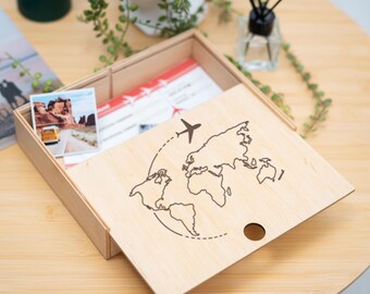 May include: A wooden box with a sliding lid. The lid features a laser-engraved design of a world map with a plane flying above it. The box is empty and ready to be filled with travel mementos.