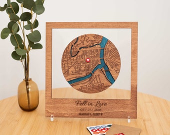 May include: A wooden map art piece with a circular map design, featuring a red heart marker. The map has blue river details and is set in a wooden frame. The text "Fell in Love" and a date are engraved below the map.