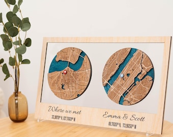 May include: Wooden framed map art featuring two circular maps with blue water details. One map has a red heart pin, the other a blue pin. Text reads "Where we met" and "Emma & Scott" with coordinates. A decorative piece.