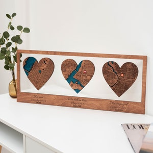 Puede incluir: Obra de arte de madera con tres mapas en forma de coraz&oacute;n. Cada coraz&oacute;n presenta un mapa de la ciudad con un elemento de agua azul turquesa. El texto debajo de cada coraz&oacute;n dice "We met December 2022 New York", "We fell in love May 2023 Niagara Falls" y "We engaged September 2023 Philadelphia".