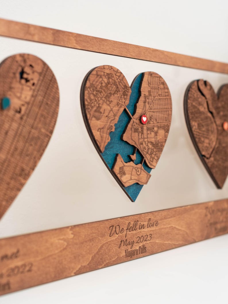 Puede incluir: Arte de mapa en forma de coraz&oacute;n de madera con un fondo azul turquesa. El mapa est&aacute; cortado con l&aacute;ser con detalles intrincados. El texto "We fell in love May 2023 Niagara Falls" est&aacute; grabado en el marco de madera. Una pieza &uacute;nica.